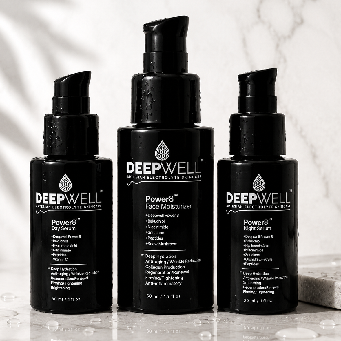 Three DEEPWELL skincare bottles on a reflective marble surface with a marble wall background. The center bottle is a black black-violet pump bottle labeled 'Powered Face Moisturizer', flanked by two black pump bottles labeled 'Powered Day Serum' and 'Powered Night Serum'.