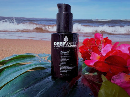 DeepWell Power8 Day Serum 30ml bottle on a beach with tropical flowers and ocean waves — powered by artesian electrolyte water